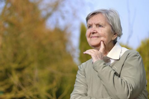 Senior woman looking and smiling in garden on blue sky.