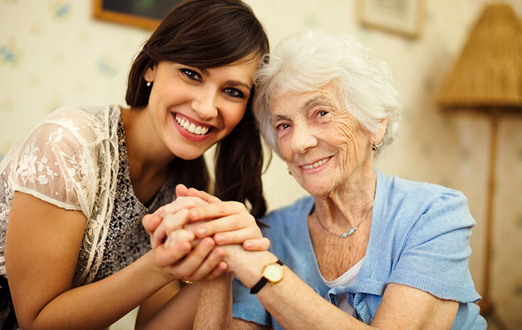 A professional companion care provider holds hands with an elderly client.