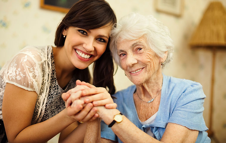 A professional companion care provider in Syracuse holds hands with an elderly client.