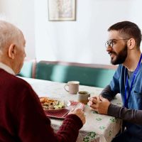 caregiver-encouraging-senior-man-to-eat