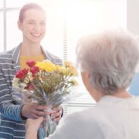Caregiver giving flowers to senior woman