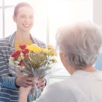 Caregiver giving flowers to senior woman