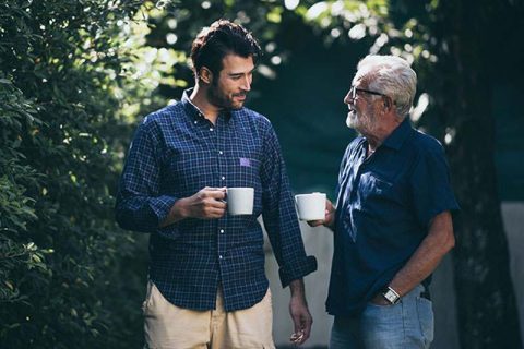 Adult son and senior father outside drinking coffee