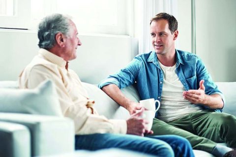 The adult child of a senior and the senior parent sit on the couch discussing home care options.