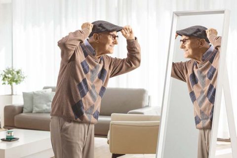 A senior looks in the mirror as he gets dressed with adaptive clothing for older adults.