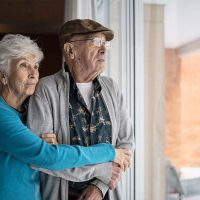 An older adult who understands overcoming resentment while caring for your spouse holds her husband as they look out the window.
