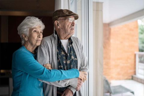 An older adult who understands overcoming resentment while caring for your spouse holds her husband as they look out the window.