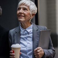 A woman caring for aging family members smiles at work while holding a cup of coffee.