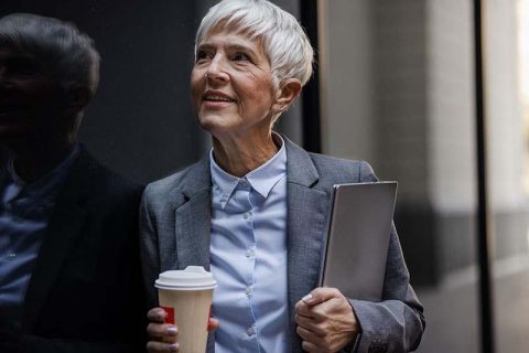 A woman caring for aging family members smiles at work while holding a cup of coffee.